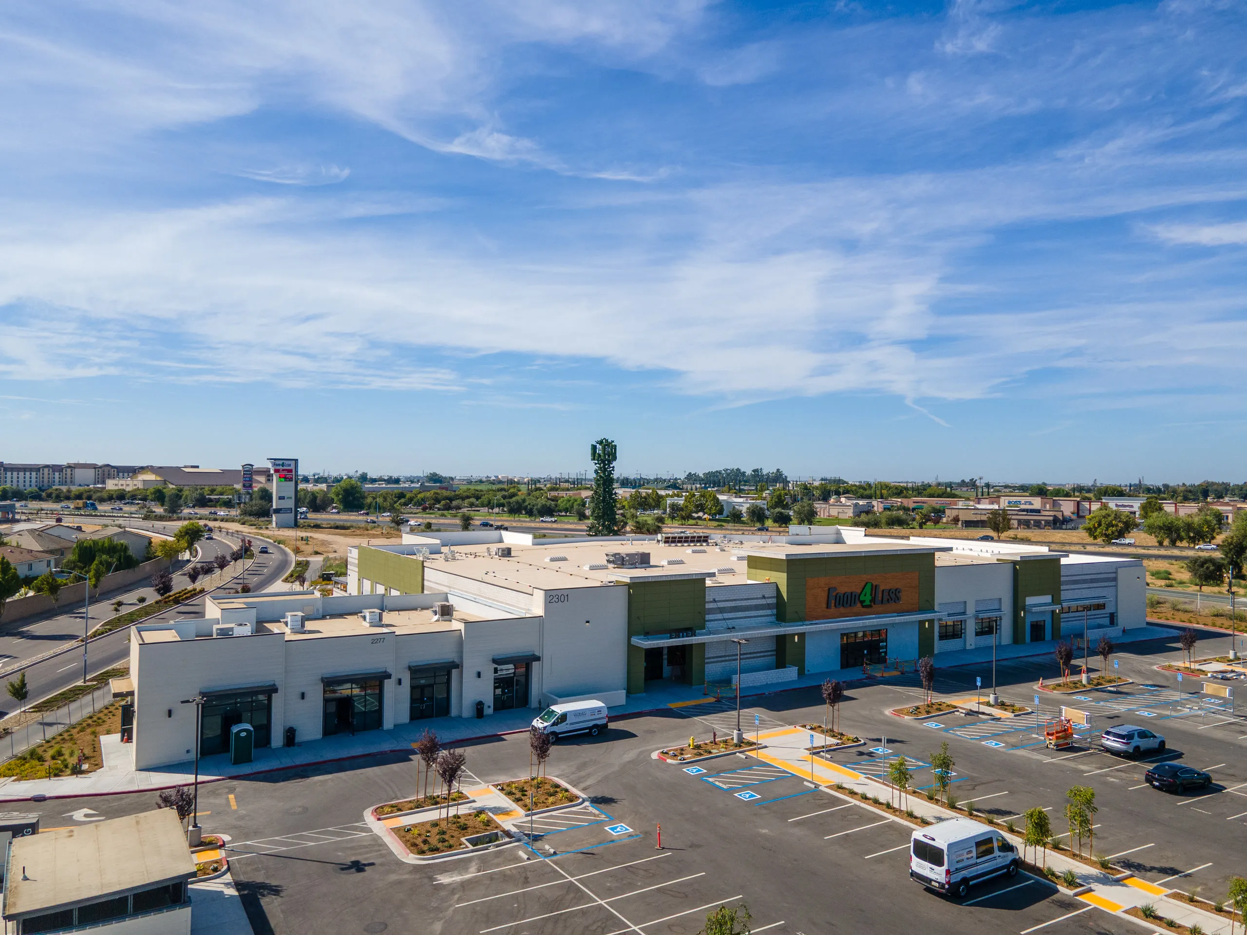 Food 4 Less and the Shops H building side by side, with Highway 120 and the pylon sign in the background