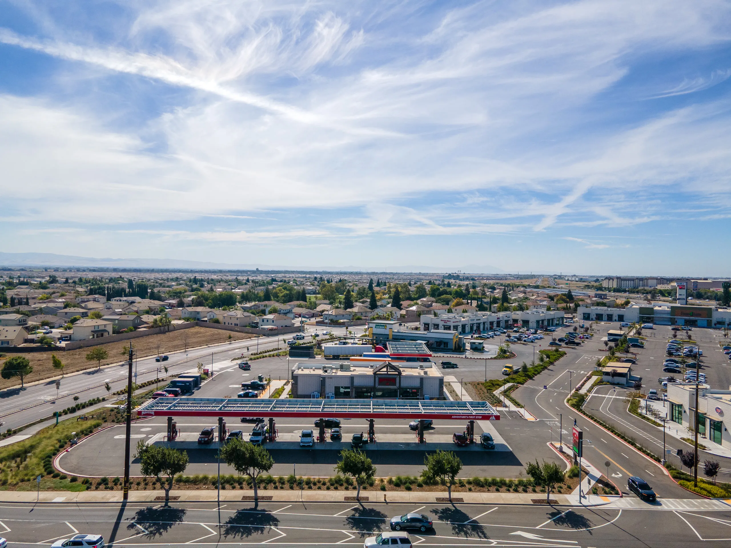 Maverik fuel canopy and convenience store at the Highway 120 and Airport Way corner, with the center behind