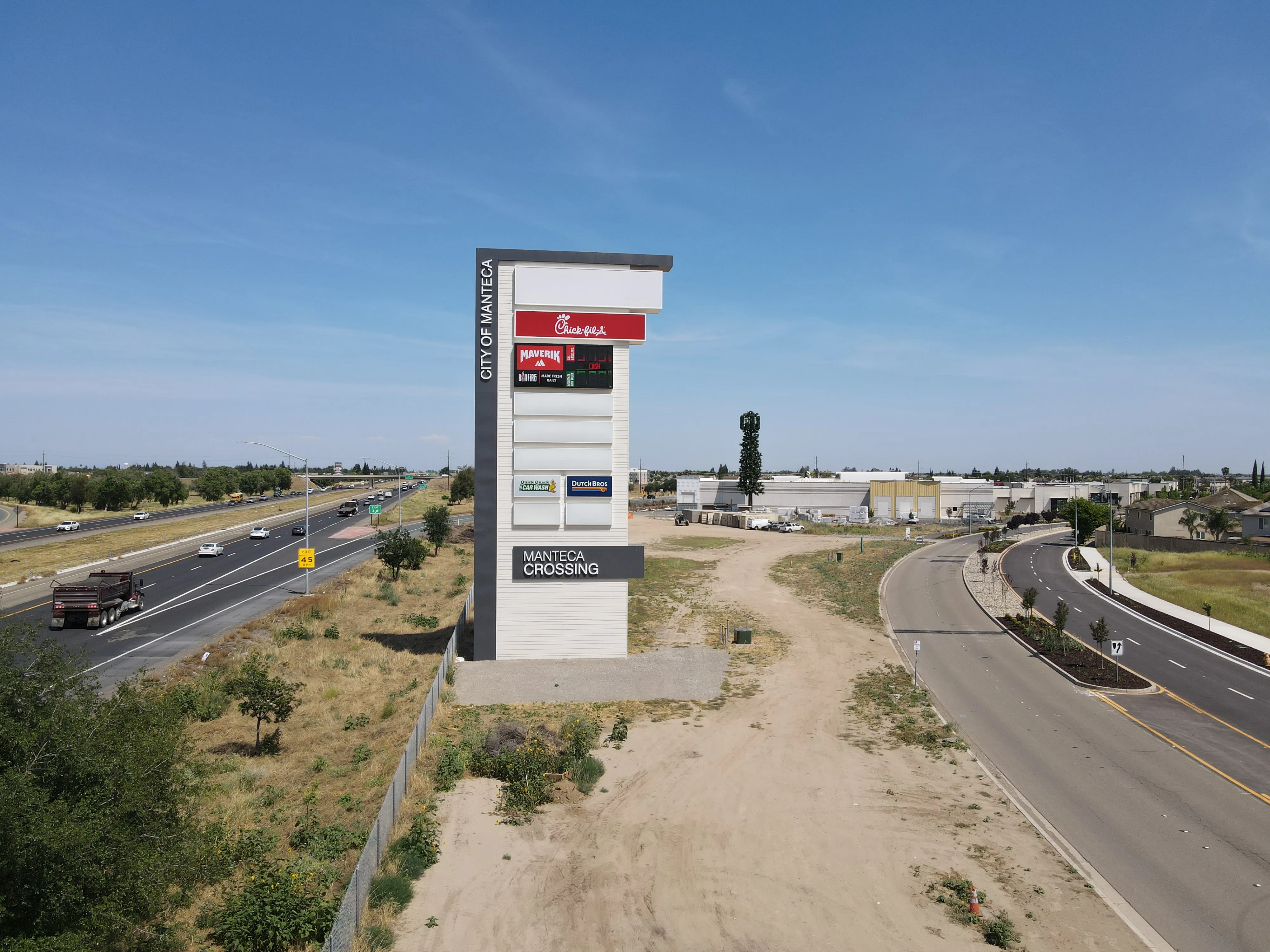 Manteca Crossing pylon sign along Highway 120 with Chick-fil-A, Maverik, Quick Quack Car Wash, and Dutch Bros panels