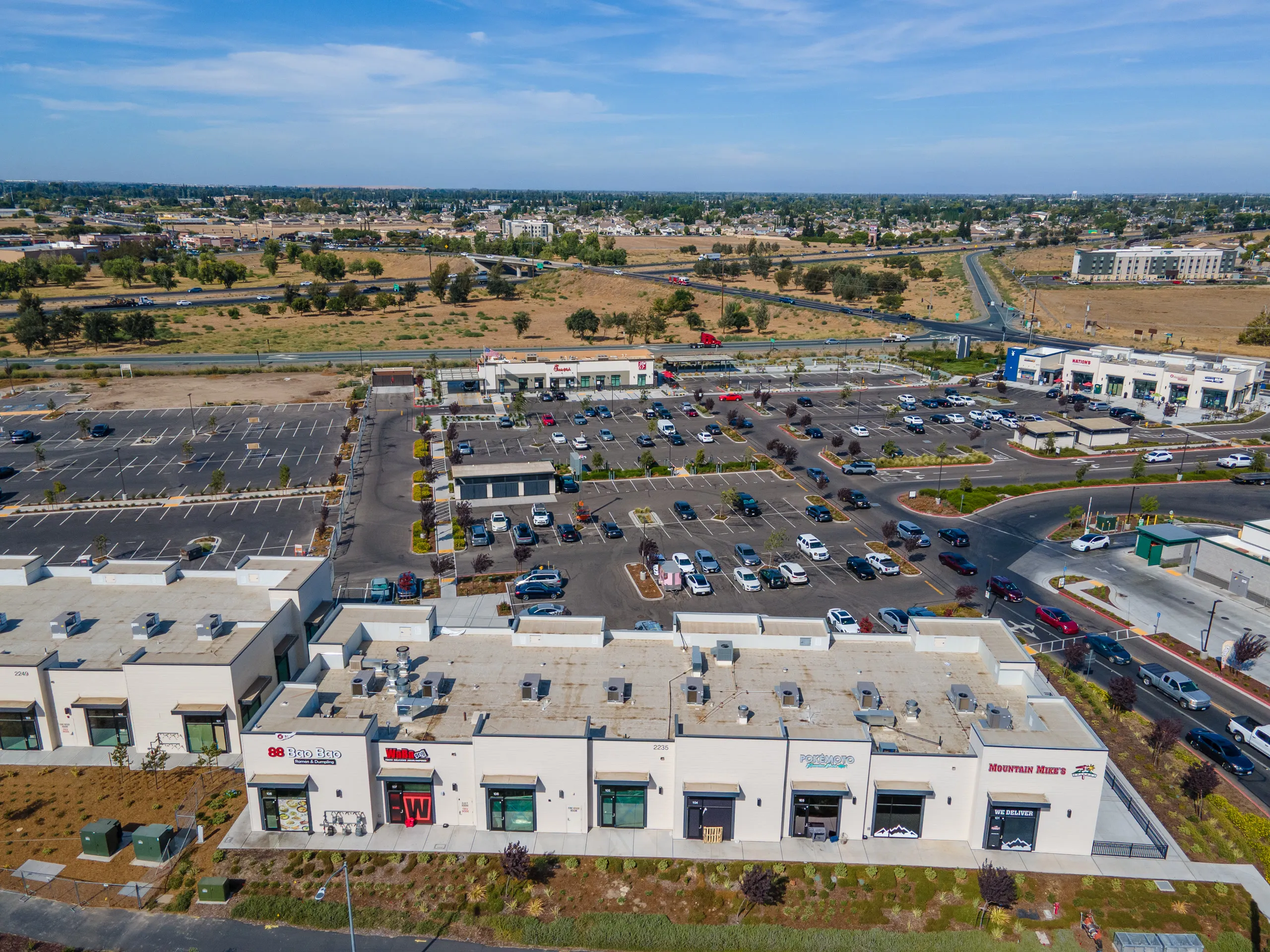 Aerial view over the Shops A rooftop — 88 Bao Bao, Wingstop, and Mountain Mike's Pizza — toward the parking field and Highway 120